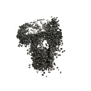 May include: A close-up of a pile of black, irregularly shaped, small, rough, and shiny particles. The particles are scattered on a white background.