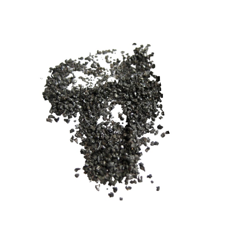 May include: A close-up of a pile of black, irregularly shaped, small, rough, and shiny particles. The particles are scattered on a white background.