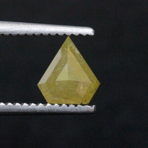 May include: A yellow diamond with a unique, faceted cut. The diamond is held in place by a pair of tweezers.