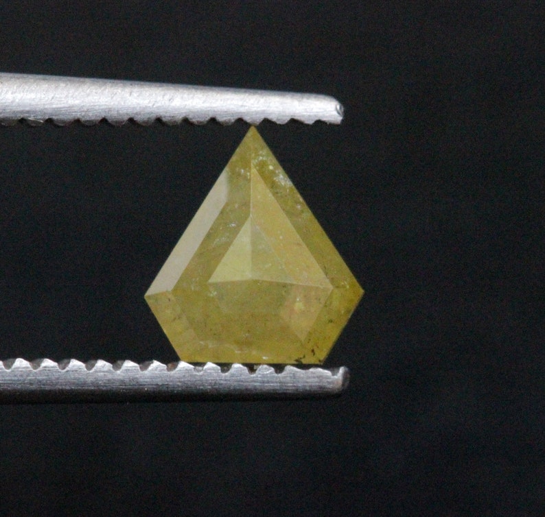 May include: A yellow diamond with a unique, faceted cut. The diamond is held in place by a pair of tweezers.