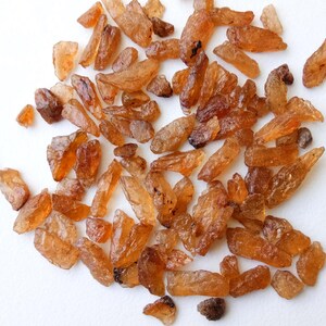 May include: A collection of small, rough, orange-brown gemstones. The gemstones are irregularly shaped and have a translucent appearance.