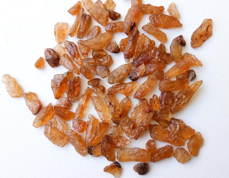 May include: A collection of small, rough, orange-brown gemstones. The gemstones are irregularly shaped and have a translucent appearance.