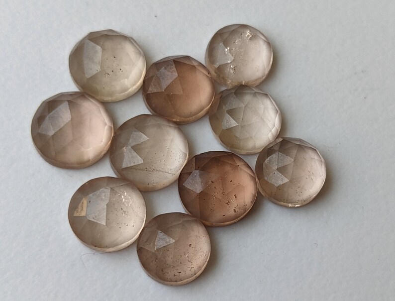 Puede incluir: Diez piedras preciosas redondas, facetadas, transl&uacute;cidas, de color marr&oacute;n claro. Las piedras preciosas tienen una calidad ligeramente iridiscente.
