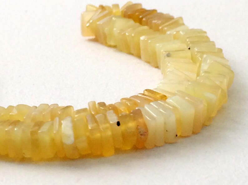 May include: A strand of yellow and white opal beads, each bead is a rectangular shape with a slightly pointed edge.