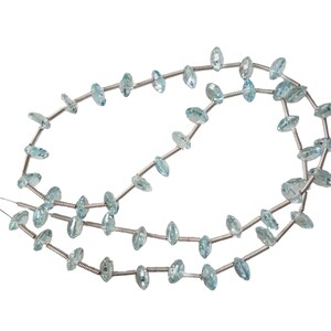 May include: A strand of light blue aquamarine gemstone beads strung on silver wire. The beads are faceted and have a marquise shape.