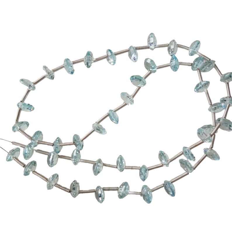 May include: A strand of light blue aquamarine gemstone beads strung on silver wire. The beads are faceted and have a marquise shape.