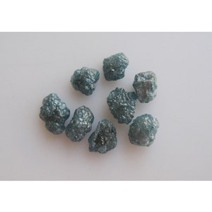 May include: A collection of eight rough, blue-grey diamonds. The diamonds are various sizes and shapes, and have a natural, unpolished finish.