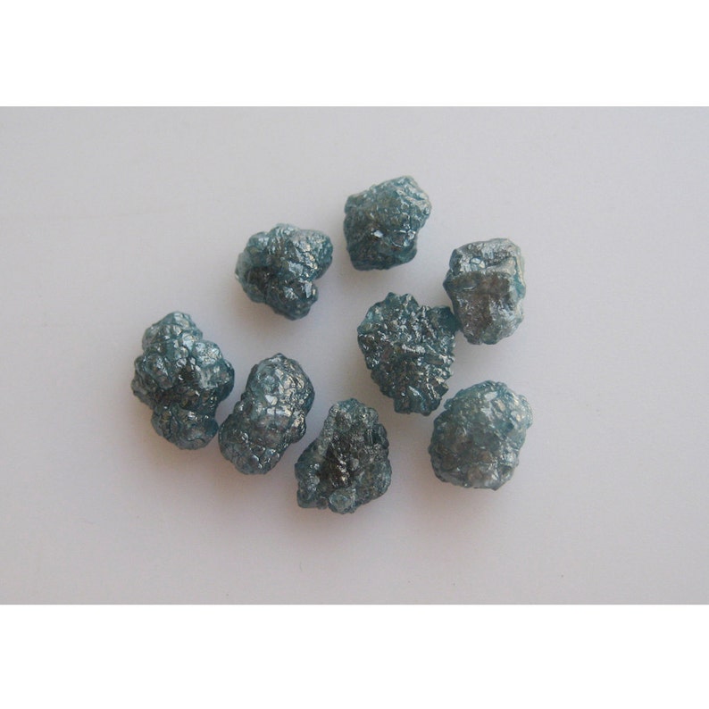 May include: A collection of eight rough, blue-grey diamonds. The diamonds are various sizes and shapes, and have a natural, unpolished finish.