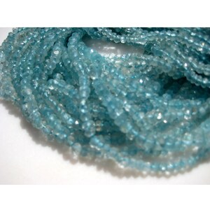 May include: A strand of light blue aquamarine beads. The beads are faceted and have a slightly irregular shape. The beads are strung on a clear thread.