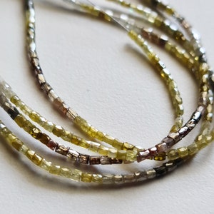 May include: A strand of light green, brown, and grey diamond beads. The beads are faceted and have a square shape.