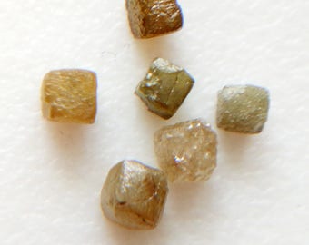 Puede incluir: Seis pequeños diamantes en bruto de forma cúbica, de color marrón y verde.