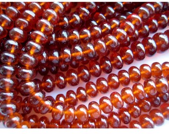 May include: A strand of smooth, round, reddish-brown gemstone beads. The beads are all approximately the same size and shape, and they have a glossy finish.