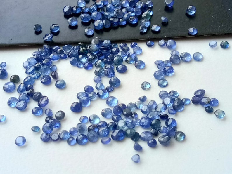May include: A scattering of small, round, blue gemstones. The gemstones are smooth and have a slightly iridescent sheen.