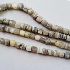 May include: A strand of white and gray agate beads with a faceted square shape. The beads are strung on a clear cord.