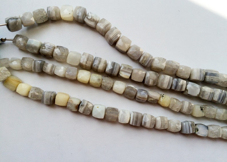May include: A strand of white and gray agate beads with a faceted square shape. The beads are strung on a clear cord.