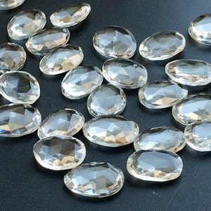Peut inclure: Une collection de cristaux de quartz transparents, facet&eacute;s et de forme ovale. Les cristaux sont dispers&eacute;s sur une surface gris fonc&eacute;.