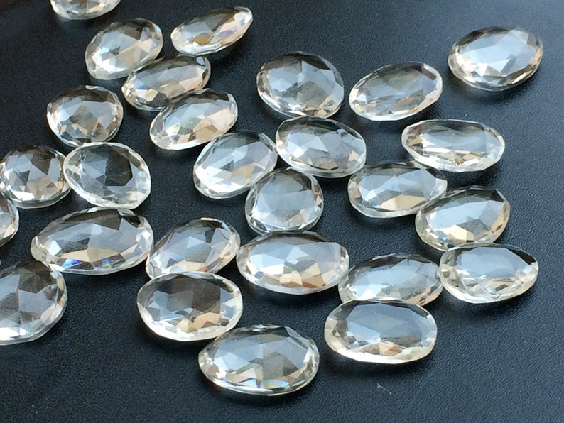 Peut inclure: Une collection de cristaux de quartz transparents, facet&eacute;s et de forme ovale. Les cristaux sont dispers&eacute;s sur une surface gris fonc&eacute;.
