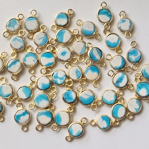 Può includere: Una collezione di perline rotonde in pietra turchese e bianca con anelli di salto dorati. Le perline hanno un diametro di circa 10 mm.