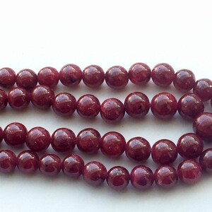 May include: A strand of deep red ruby gemstone beads. The beads are round and smooth, with a slight sheen.