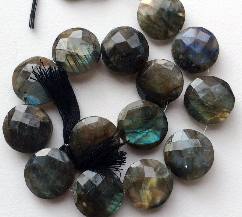 May include: A strand of faceted labradorite gemstone beads. The beads are a dark gray color with iridescent blue and green flashes. The beads are round and have a smooth, polished finish.