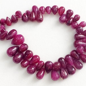 May include: A strand of deep pink ruby gemstone beads in a pear shape. The beads are strung on a thin wire and are arranged in a circular pattern.