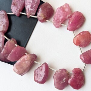 May include: A strand of pink ruby gemstone beads, each bead is irregularly shaped and polished, strung on silver wire.