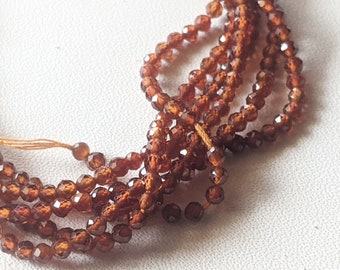 May include: A strand of brown faceted gemstone beads. The beads are strung on a thin thread and are approximately 4mm in diameter.