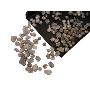 May include: A close-up of a pile of small, rough, pink and gray diamonds. The diamonds are spilling out of a black tray.