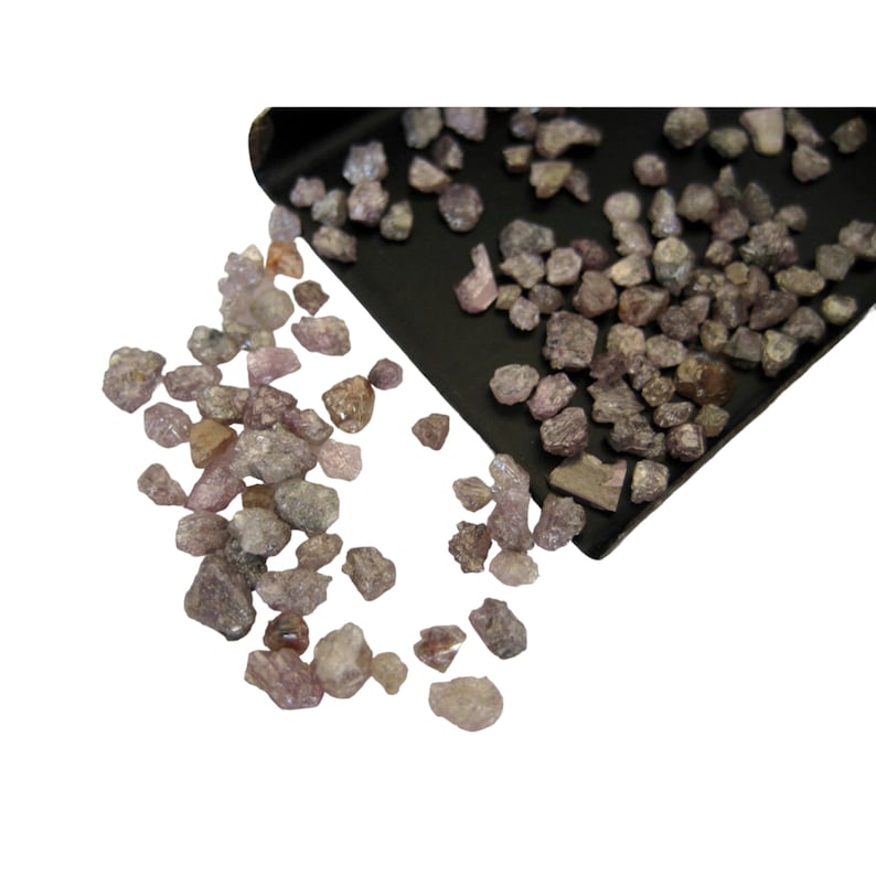May include: A close-up of a pile of small, rough, pink and gray diamonds. The diamonds are spilling out of a black tray.