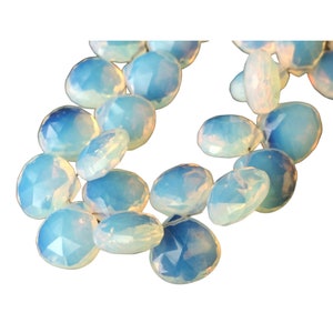 May include: A collection of faceted, oval-shaped beads in shades of pale blue and white. The beads have a translucent, opalescent appearance, with a subtle shimmer. The arrangement suggests they are strung together, possibly for jewelry making.