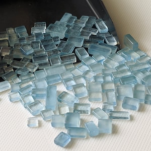 Könnte beinhalten: Eine große Menge kleiner, rechteckiger, hellblauer Glasfliesen. Die Fliesen sind auf einer weißen Oberfläche verstreut.