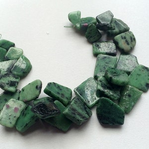 May include: A strand of green and black gemstone beads. The beads are irregularly shaped and have a mottled appearance.