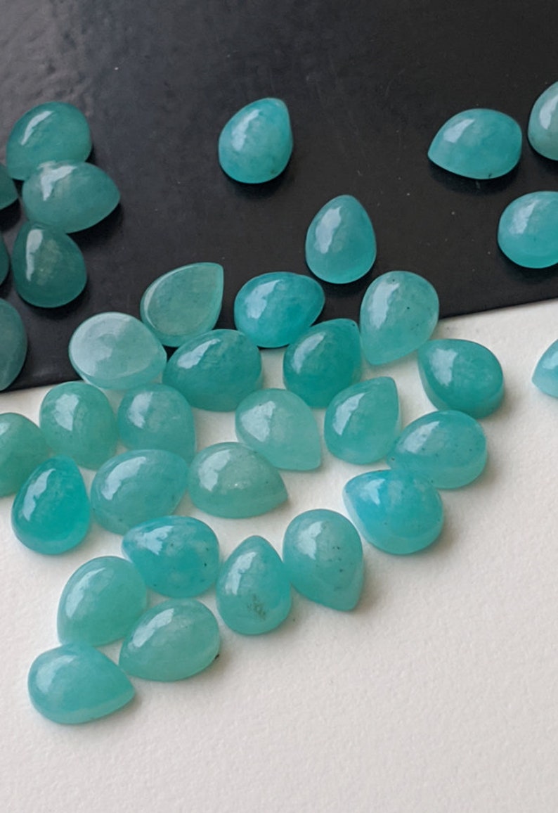 May include: A collection of loose, teardrop-shaped cabochons in a vibrant turquoise-blue color. These polished gemstones feature a smooth, rounded surface and a flat back, displaying subtle natural variations in their opaque, solid color.