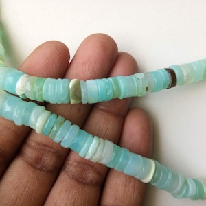 May include: A strand of light blue opal beads, with a few darker blue and white beads interspersed. The beads are all round and have a smooth, polished finish.