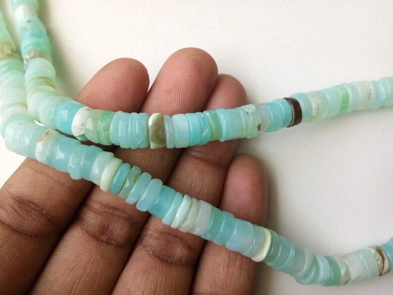 May include: A strand of light blue opal beads, with a few darker blue and white beads interspersed. The beads are all round and have a smooth, polished finish.