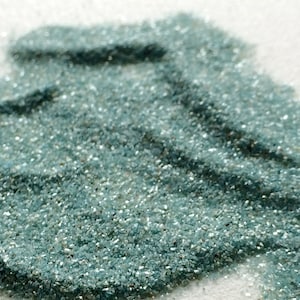 May include: A close-up of a pile of teal blue glitter. The glitter is very fine and has a slight shimmer to it.