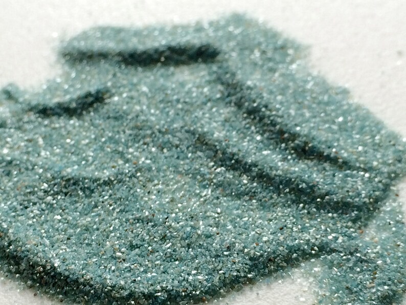 May include: A close-up of a pile of teal blue glitter. The glitter is very fine and has a slight shimmer to it.