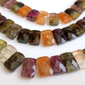 Puede incluir: Una hebra de piedras preciosas facetadas, rectangulares y multicolores. Las piedras son de tonos verdes, marrones, rosas y naranjas. Las piedras están enhebradas en un hilo fino de color rosa.