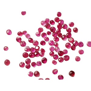 May include: A scattering of faceted, round rubies in varying shades of red and pink against a white background. The gemstones are scattered, showcasing their polished surfaces and natural color variations. Ideal for jewelry making or collecting.