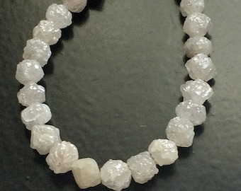 Könnte beinhalten: Eine Kette aus weißen, rohen Diamantperlen. Die Perlen sind alle unterschiedlich groß und geformt und auf einem durchsichtigen Faden aufgefädelt.