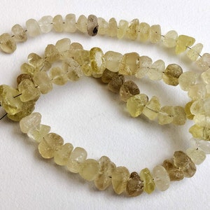 May include: A strand of light yellow and brown gemstone beads. The beads are irregularly shaped and have a rough, natural texture.