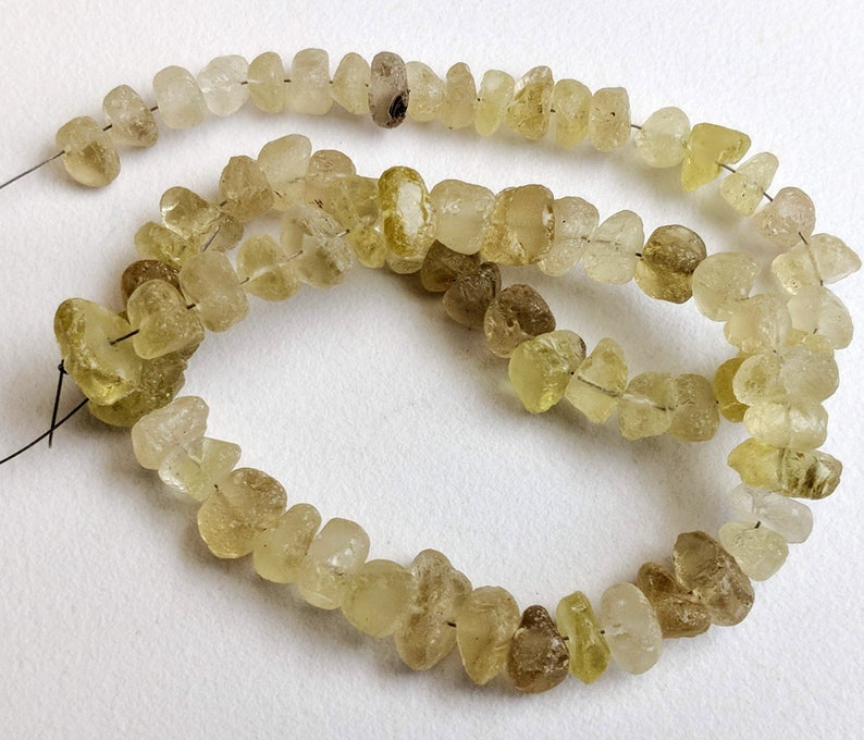 May include: A strand of light yellow and brown gemstone beads. The beads are irregularly shaped and have a rough, natural texture.