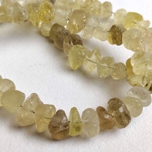 May include: A strand of light yellow and brown gemstone beads. The beads are irregular in shape and have a translucent appearance.