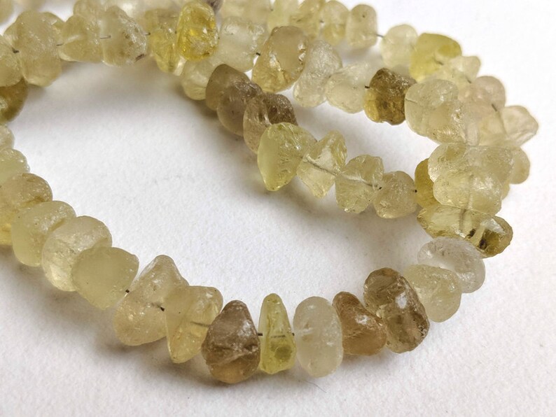 May include: A strand of light yellow and brown gemstone beads. The beads are irregular in shape and have a translucent appearance.
