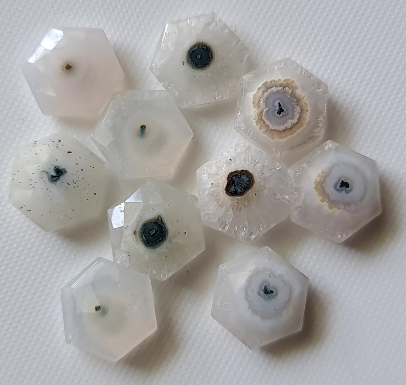 May include: Ten white, hexagonal, agate cabochons with various patterns of black, gray, and brown inclusions. The cabochons are polished and have a smooth, glossy finish.