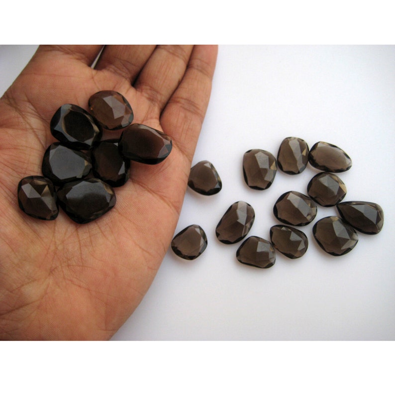 May include: A collection of smoky quartz gemstones, faceted and cut into irregular shapes. The stones are a dark brown color and have a translucent appearance.