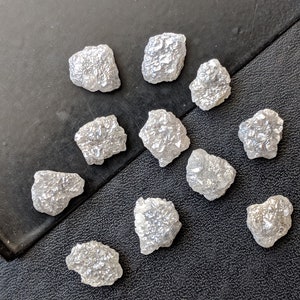 K&ouml;nnte beinhalten: Eine Sammlung von 11 rohen, wei&szlig;en, ungeschliffenen Diamanten. Die Diamanten sind in verschiedenen Gr&ouml;&szlig;en und Formen und haben ein nat&uuml;rliches, rohes Aussehen.