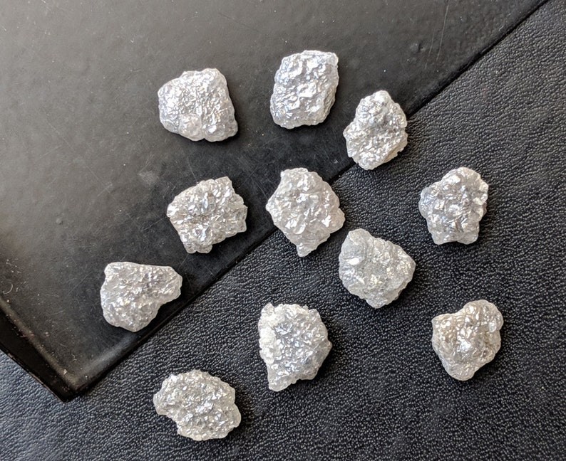 K&ouml;nnte beinhalten: Eine Sammlung von 11 rohen, wei&szlig;en, ungeschliffenen Diamanten. Die Diamanten sind in verschiedenen Gr&ouml;&szlig;en und Formen und haben ein nat&uuml;rliches, rohes Aussehen.