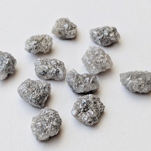 K&ouml;nnte beinhalten: Eine Sammlung von zehn rohen, grauen Diamanten. Die Diamanten sind in verschiedenen Gr&ouml;&szlig;en und Formen und haben ein nat&uuml;rliches, unpoliertes Aussehen.