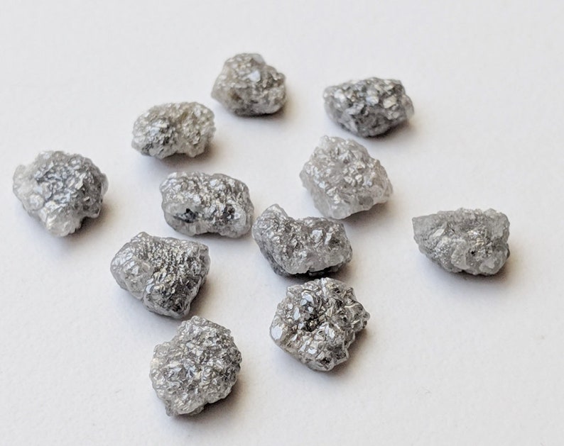 K&ouml;nnte beinhalten: Eine Sammlung von zehn rohen, grauen Diamanten. Die Diamanten sind in verschiedenen Gr&ouml;&szlig;en und Formen und haben ein nat&uuml;rliches, unpoliertes Aussehen.